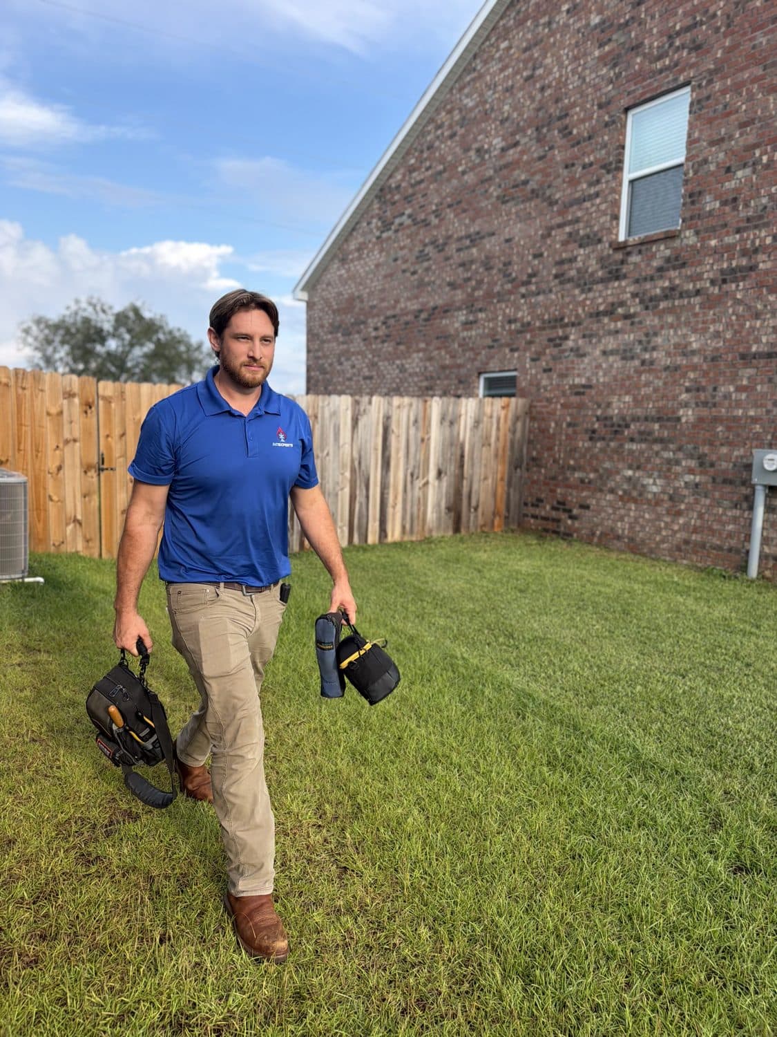 Landon Jahnke walking across a back yard carrying tool bags to an outdoor unit